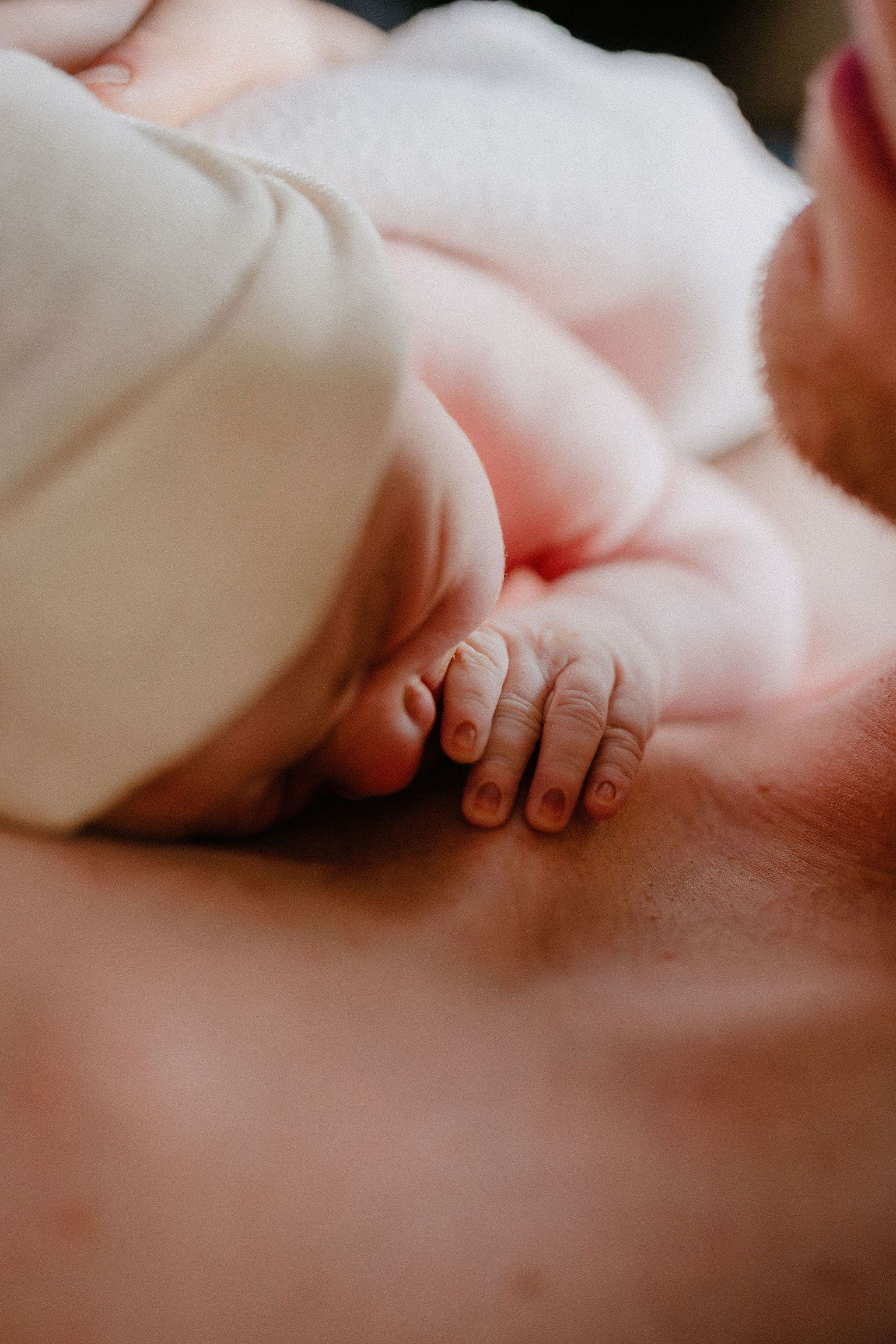 Close-up of a newborn baby's tiny hand and feet resting on a father's bare chest during skin-to-skin bonding.