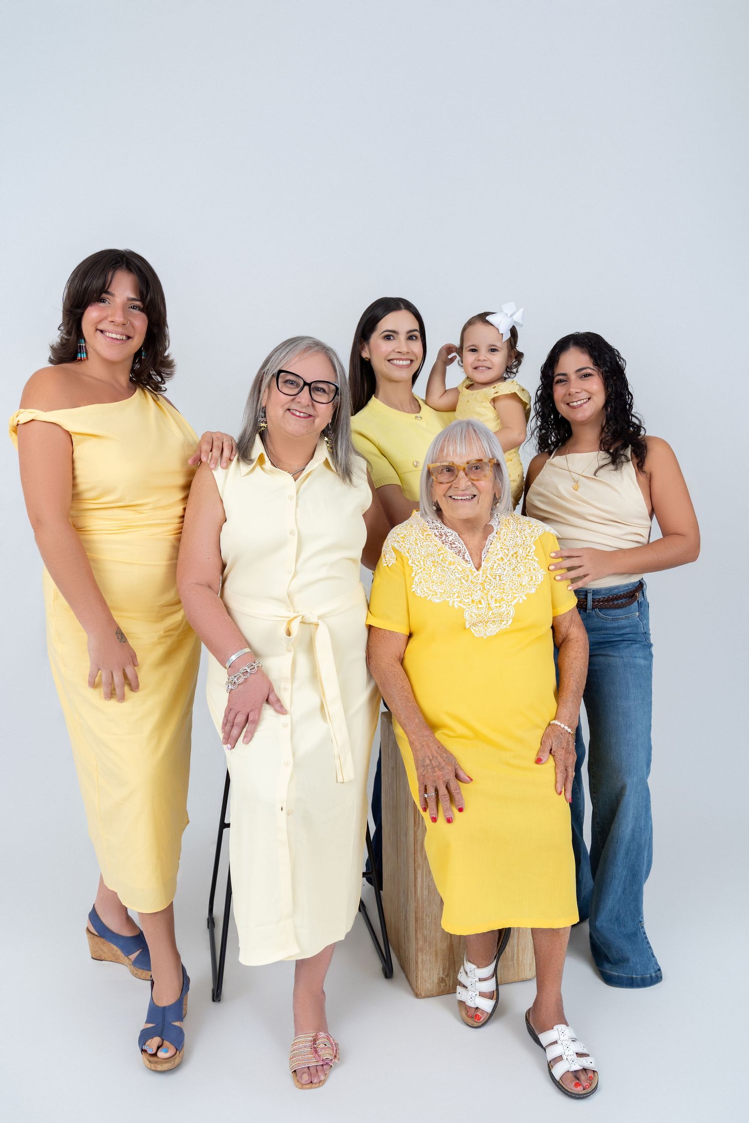 Multi-generational family of women in yellow outfits posing together, including a baby, against a white background.