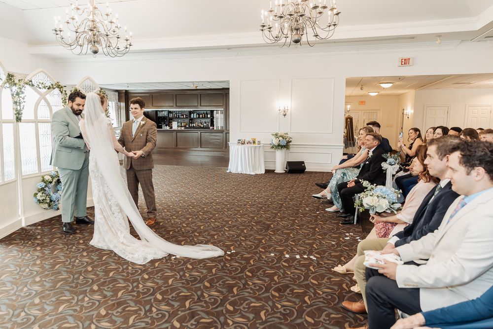 Bride and groom stand at wedding ceremony altar in elegant ballroom venue with seated guests.
