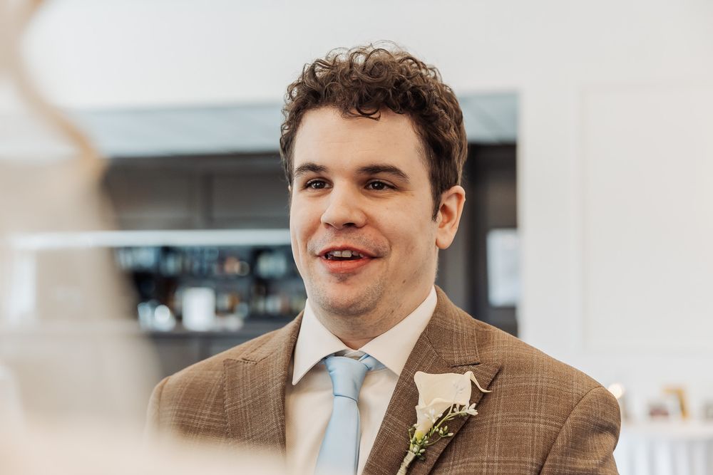 Smiling groom in brown plaid suit with boutonniere and light blue tie at wedding reception.