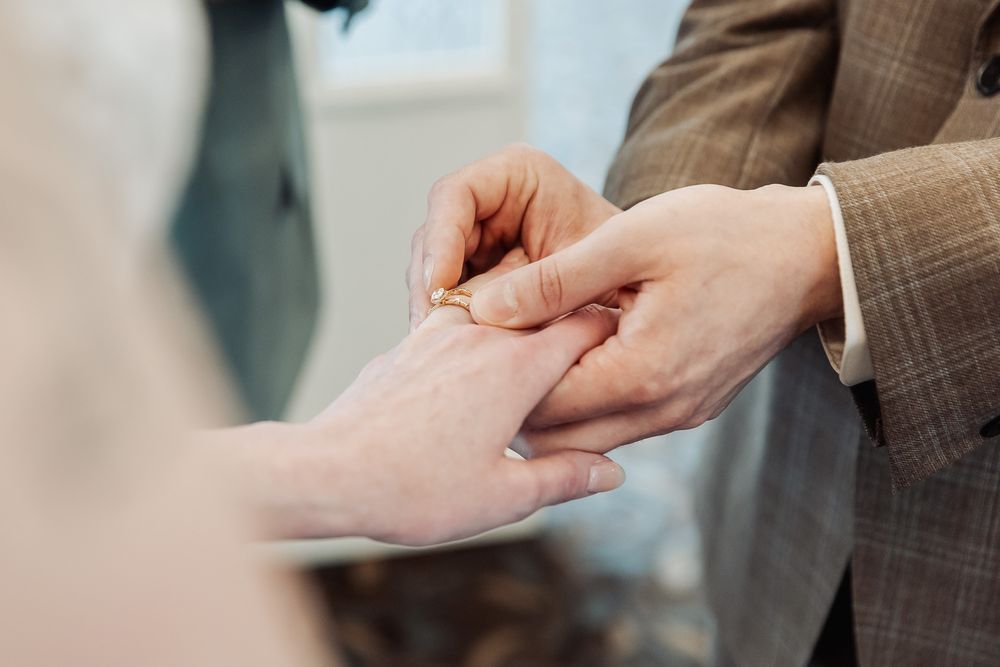 Groom places gold wedding ring on bride's finger during ring exchange ceremony.