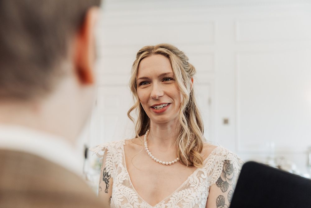 Smiling bride in lace wedding dress and pearl necklace during wedding ceremony.