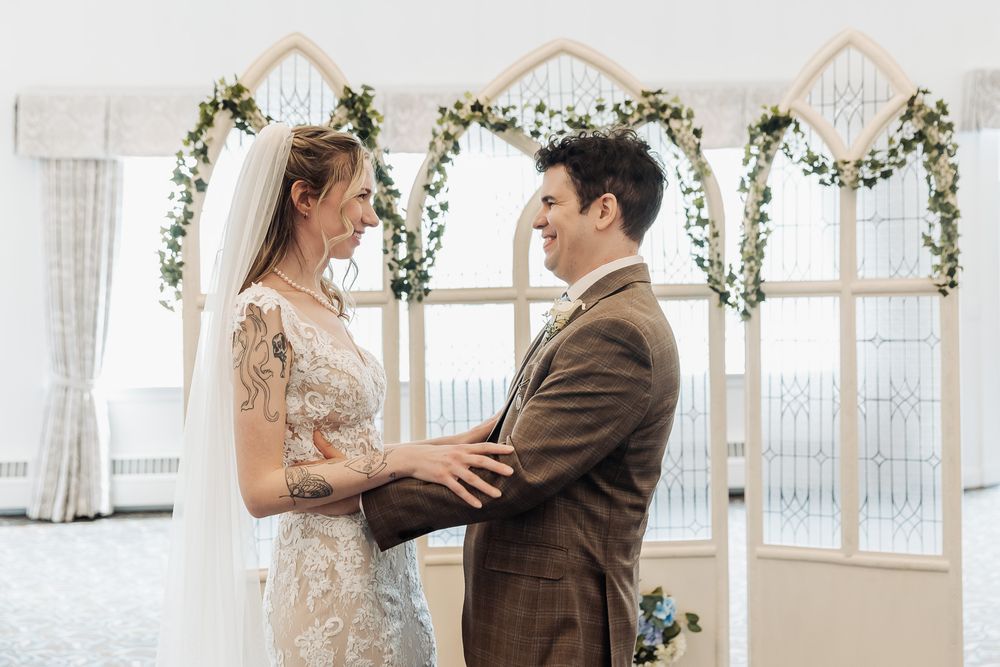 Bride and groom exchanging vows at indoor wedding ceremony with floral arch backdrop.
