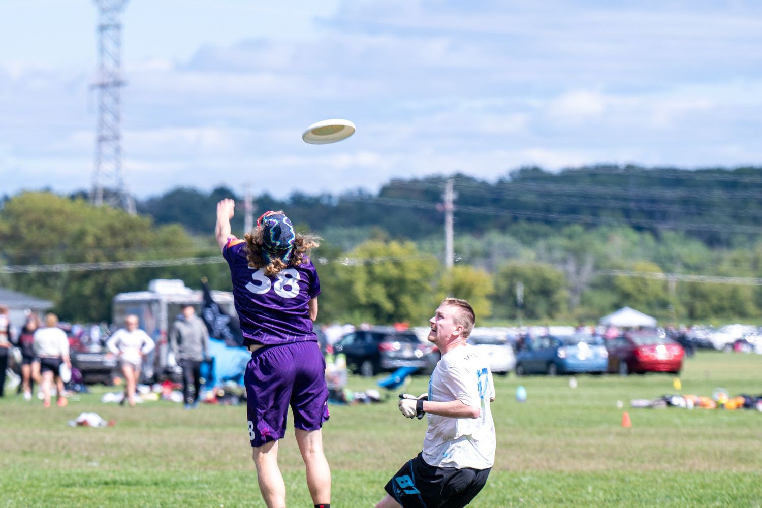 Two players compete for a frisbee catch during an outdoor ultimate frisbee tournament on a sunny day.