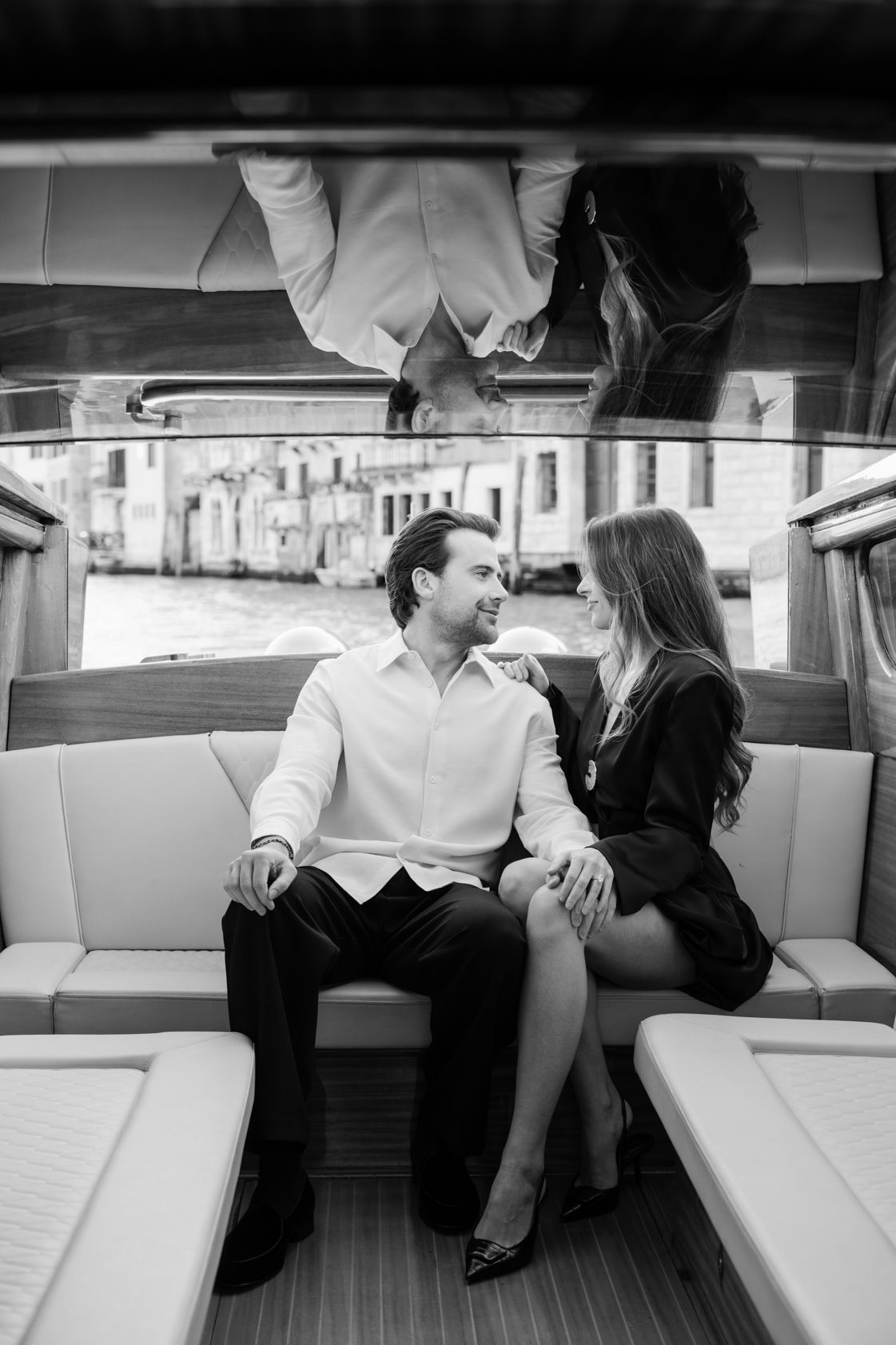 Black and white photo of an elegant couple sitting close together on a luxury boat, sharing an intimate moment in Venice.