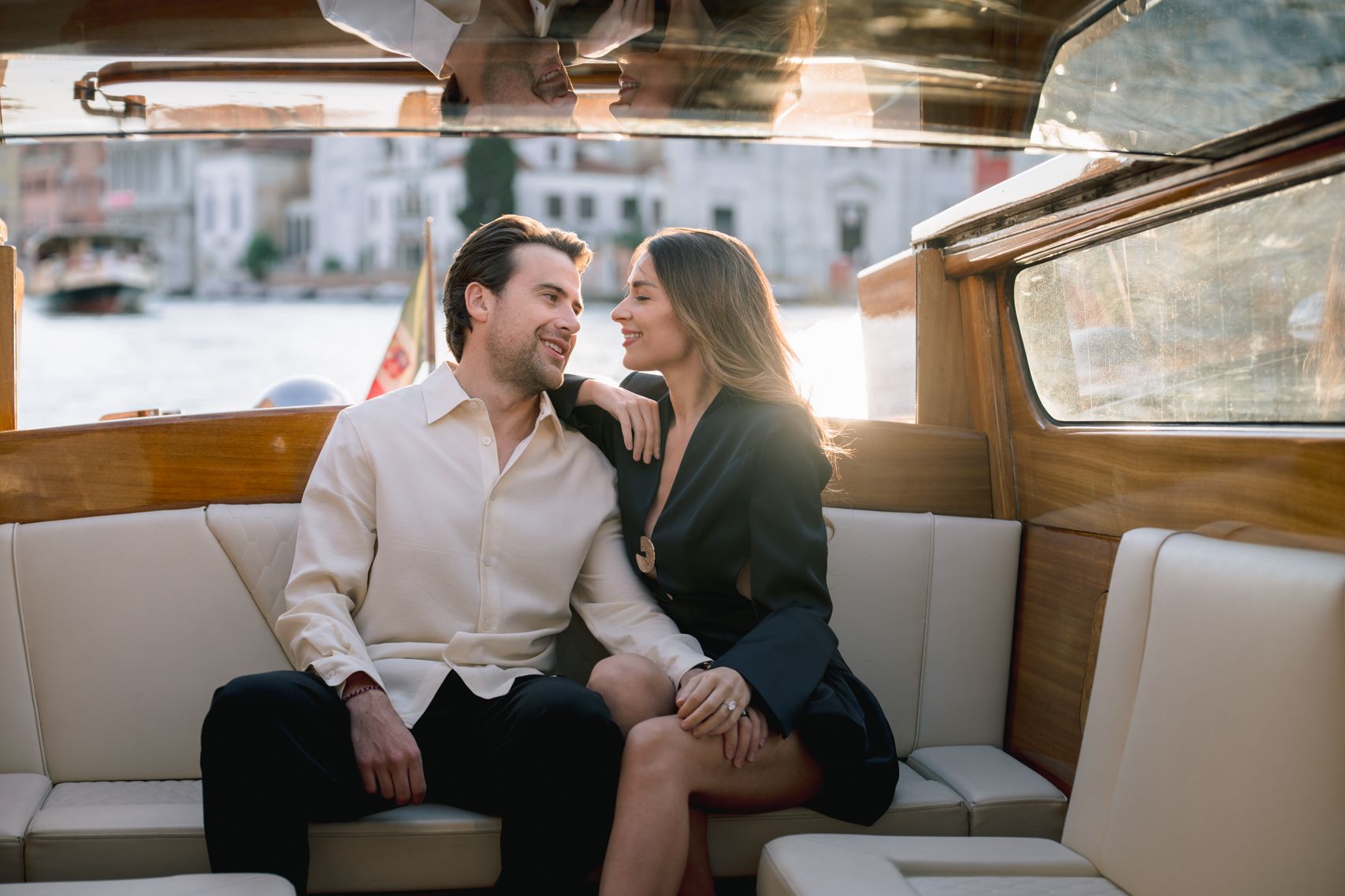 Couple sharing a romantic moment on a wooden boat in Venice, Italy, with sunlight glowing behind them.