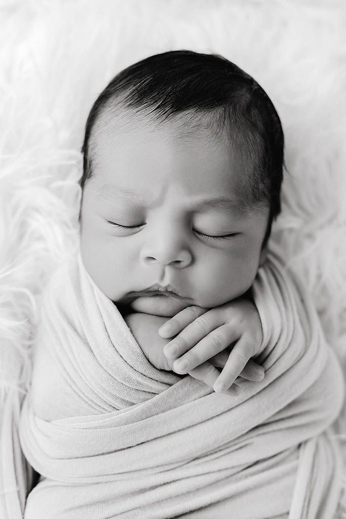 Black and white photo of a swaddled newborn baby sleeping peacefully with tiny hands visible by Murrieta newborn photographer.