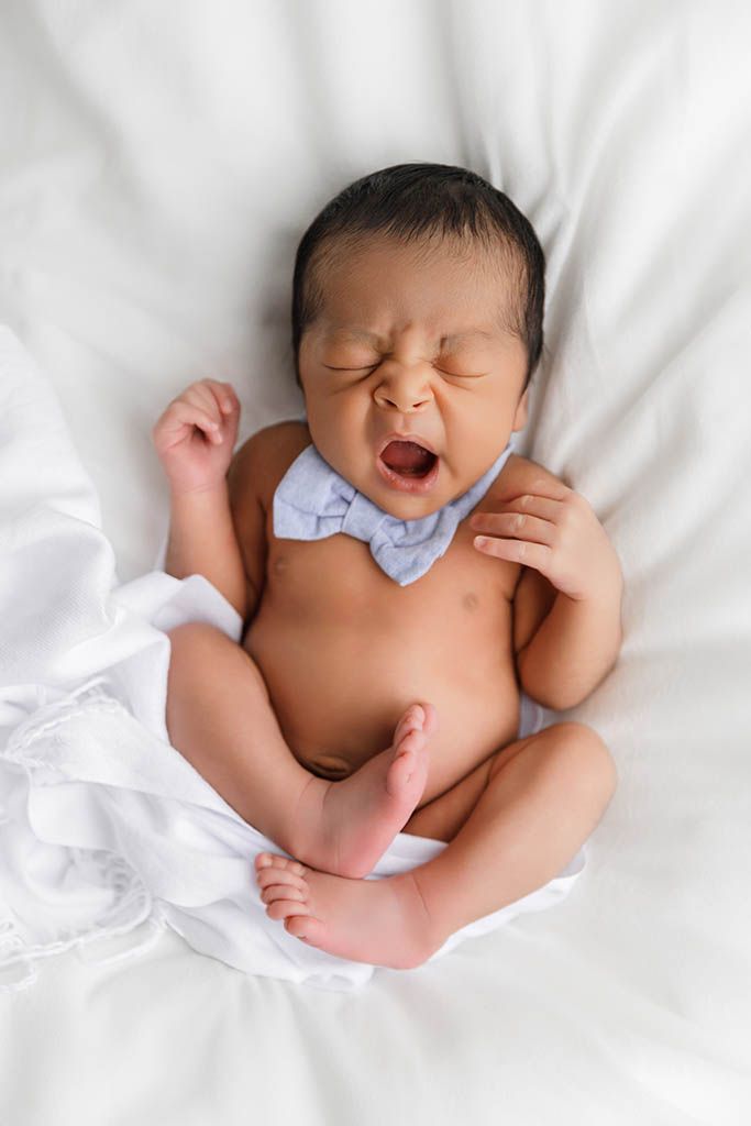 Yawning newborn baby in bow tie lying on white blanket by Murrieta newborn photographer.