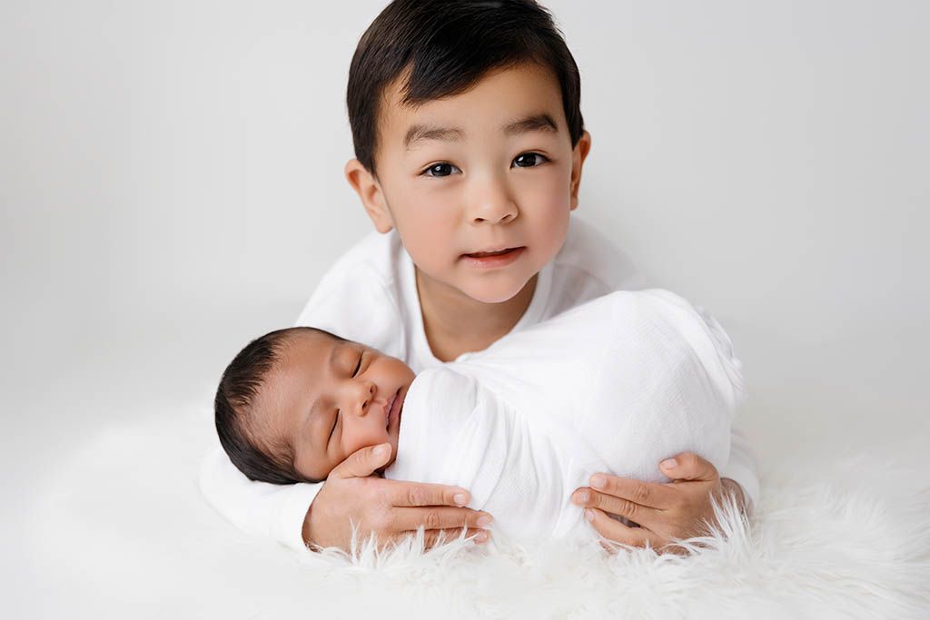 Big brother holding newborn baby brother by affordable Murrieta newborn photographer.