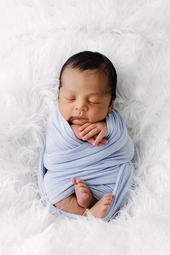 Peaceful newborn baby swaddled in a soft blue wrap, sleeping on a white fluffy blanket by Murrieta newborn photographer.