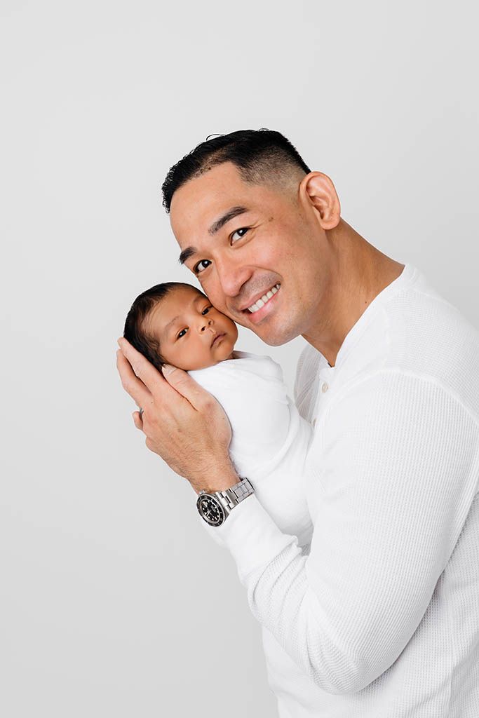 Smiling dad holding newborn son by Murrieta newborn photographer.