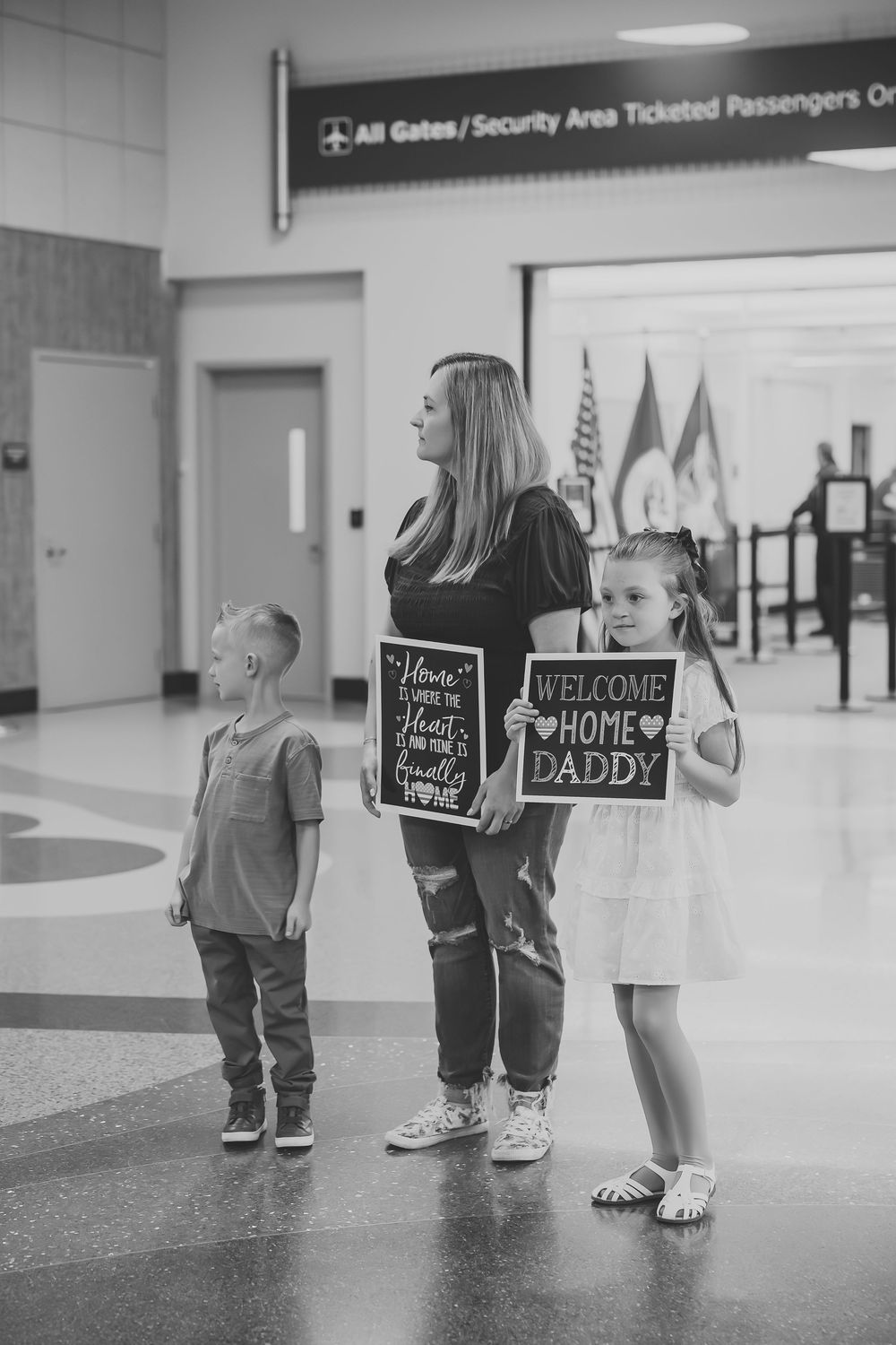 Family holding welcome home daddy signs awaiting military father's return at airport security area.