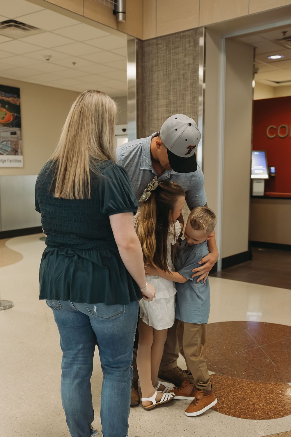Family sharing a warm embrace in a building lobby, with parents hugging two young children tenderly.