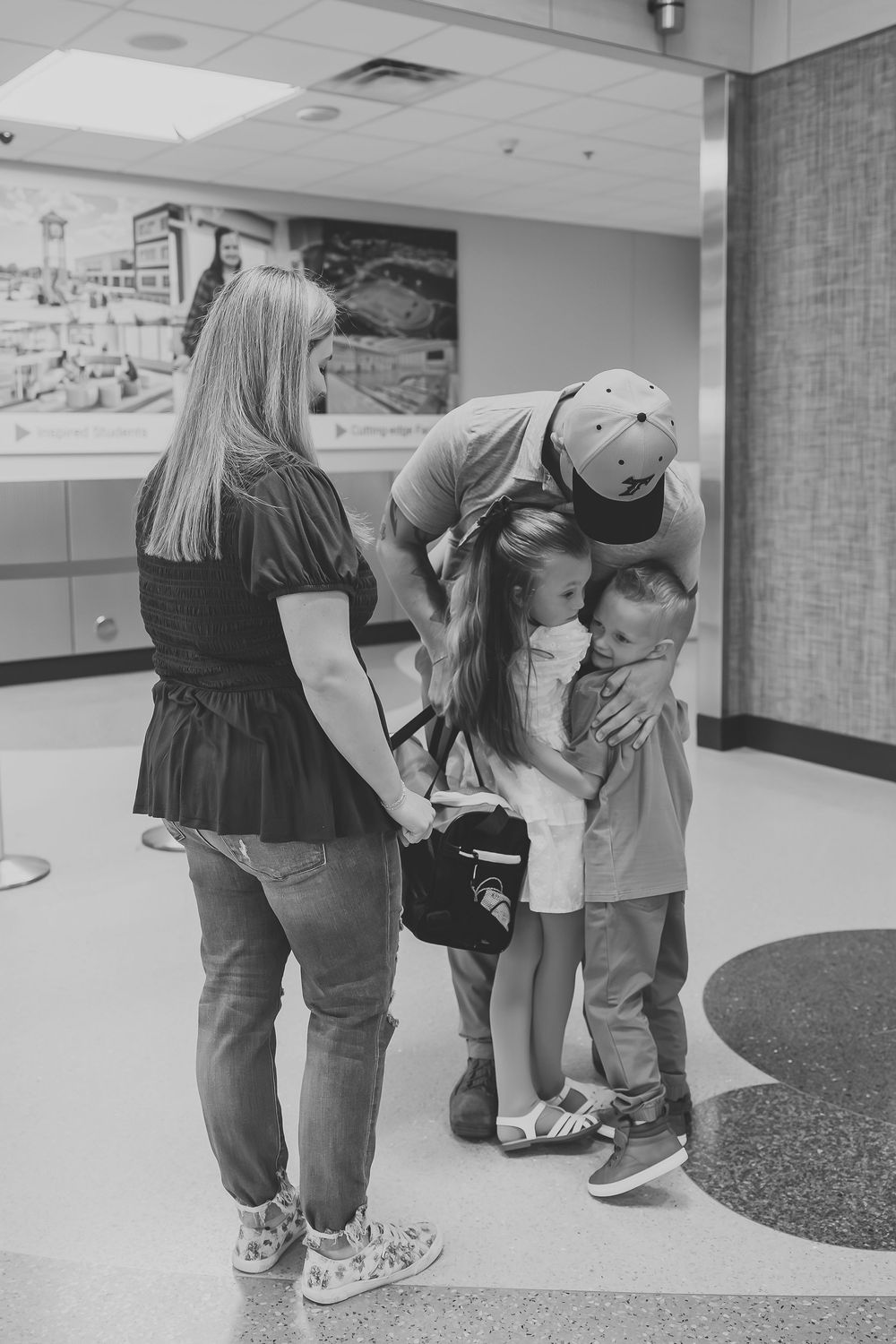 Family sharing an emotional embrace in an airport terminal, black and white photo.