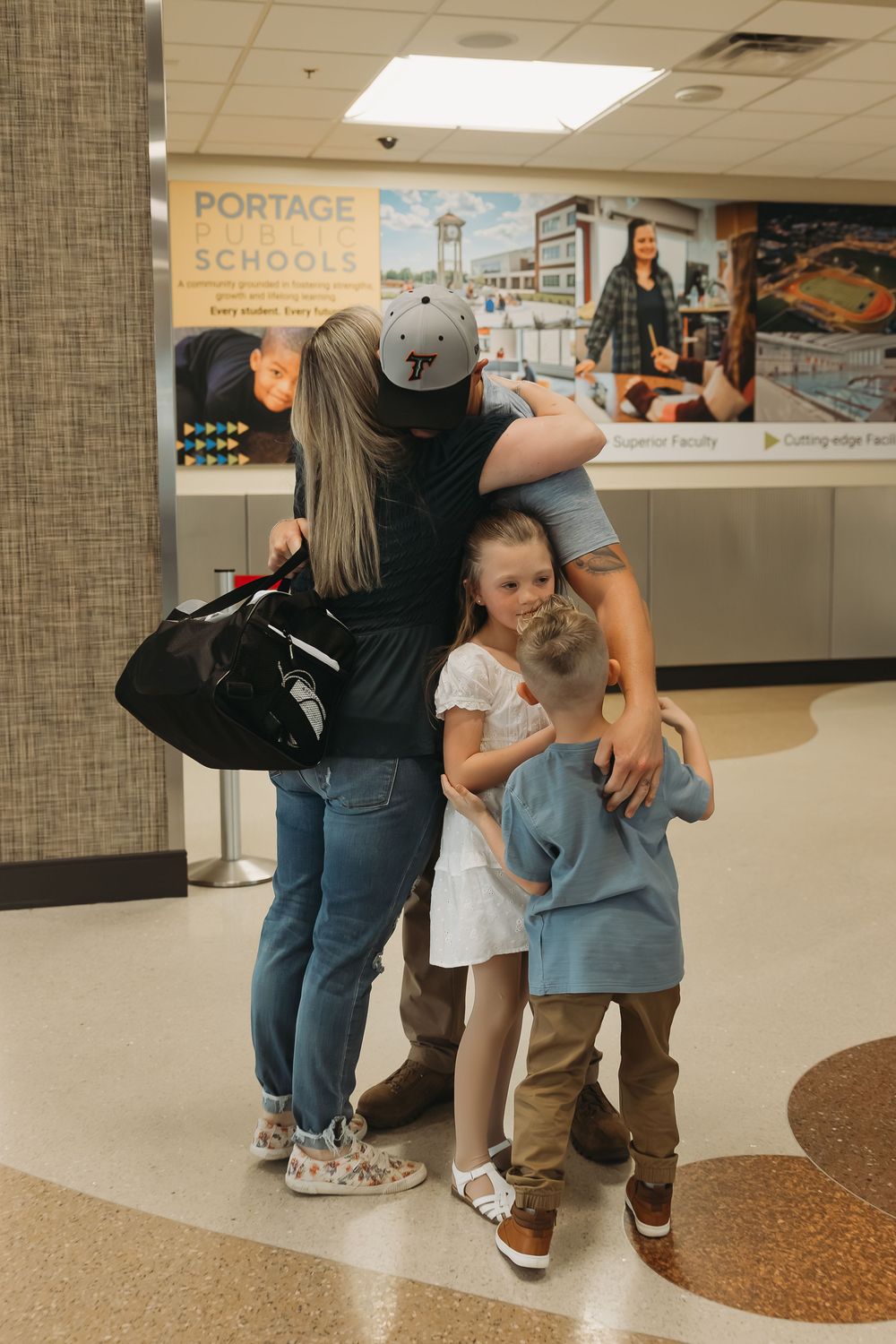 Family reunion hug at Portage Schools building with two children and parents.