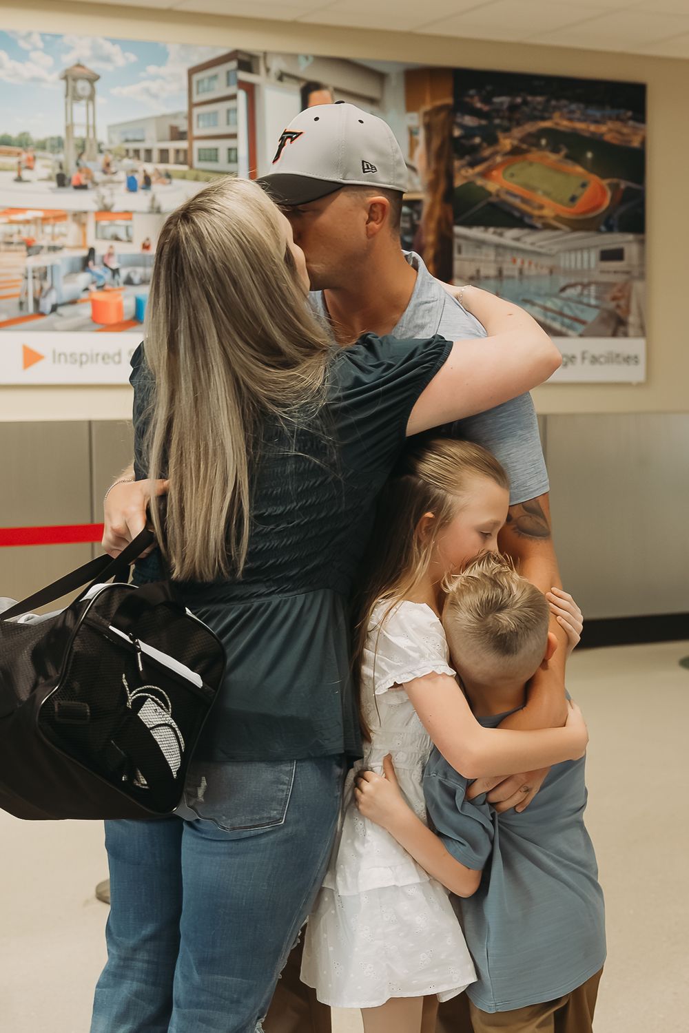 Family reunion embrace with parents kissing and children hugging in an indoor facility with inspirational wall art.