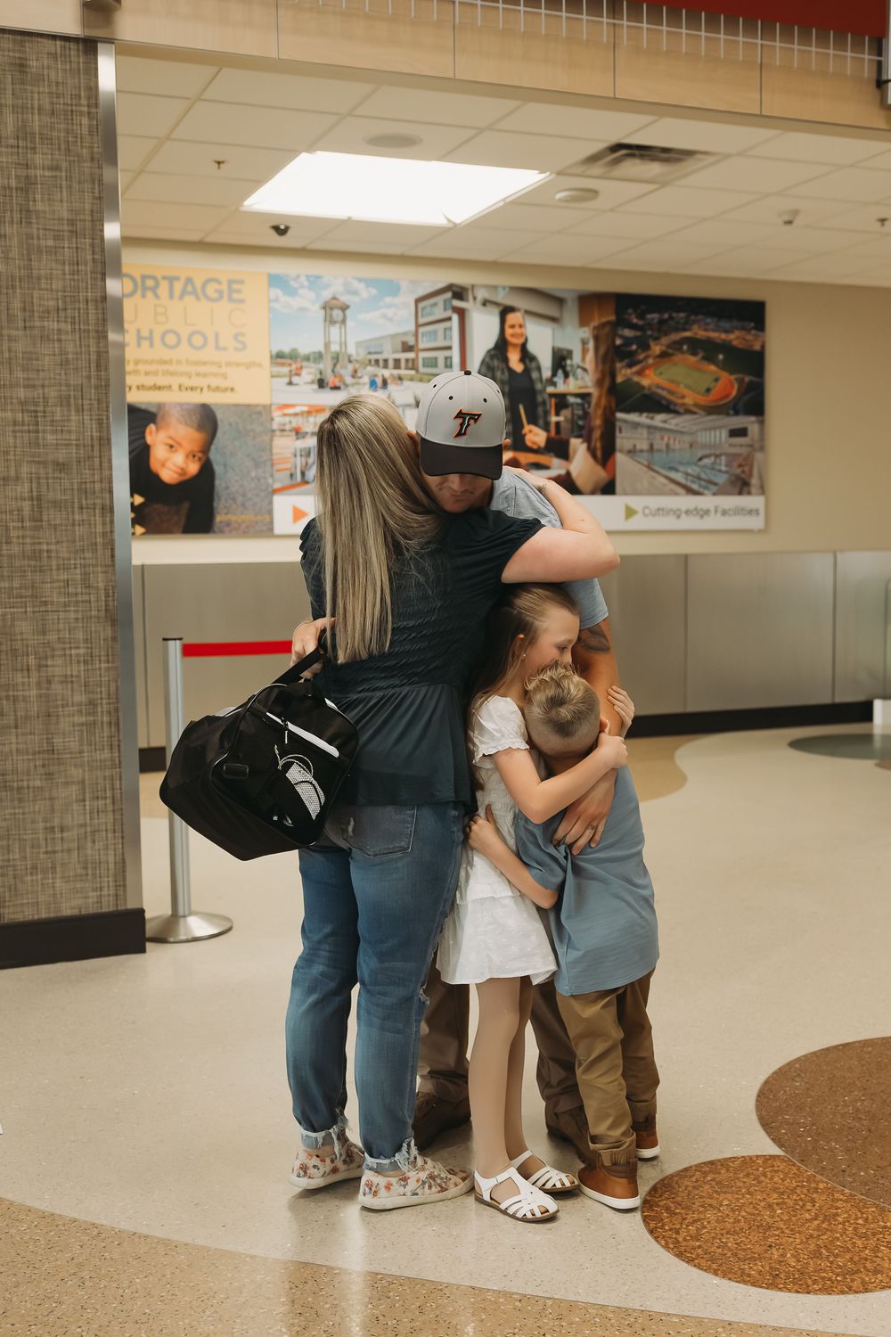 Family sharing an emotional group hug reunion at an airport terminal, with children embracing their parent.