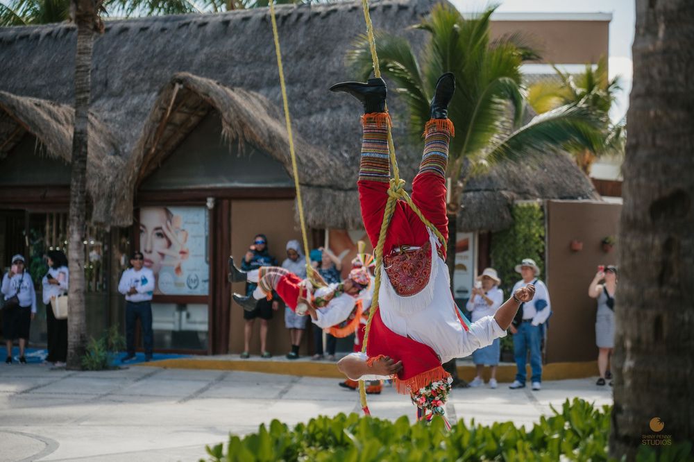 Colorful performer in traditional costume swinging upside down on ropes at a Mexican resort during a cultural show.