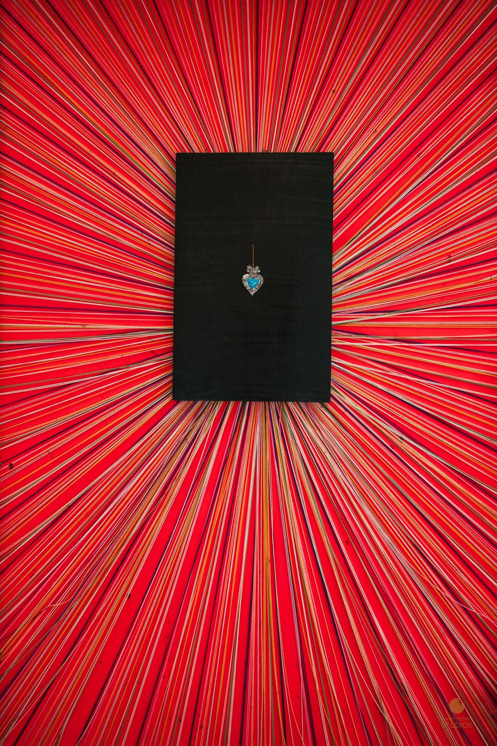 Black book with turquoise heart charm centered on a bold red radial striped background.