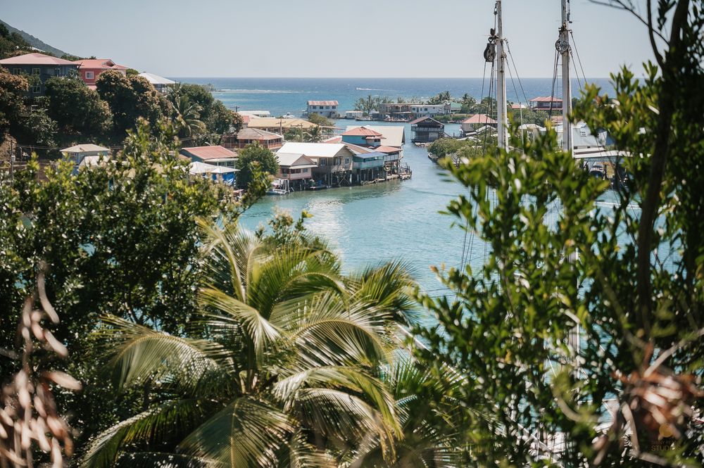 Scenic aerial view of a tropical Caribbean coastal village with colorful stilt houses along a calm blue waterway.