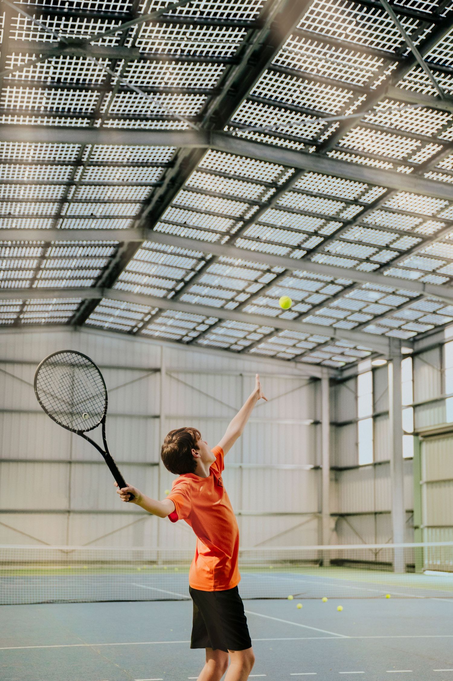 photographie d'un jeune joueur de tennis en mouvement sous des panneaux solaires installés en ombrière.