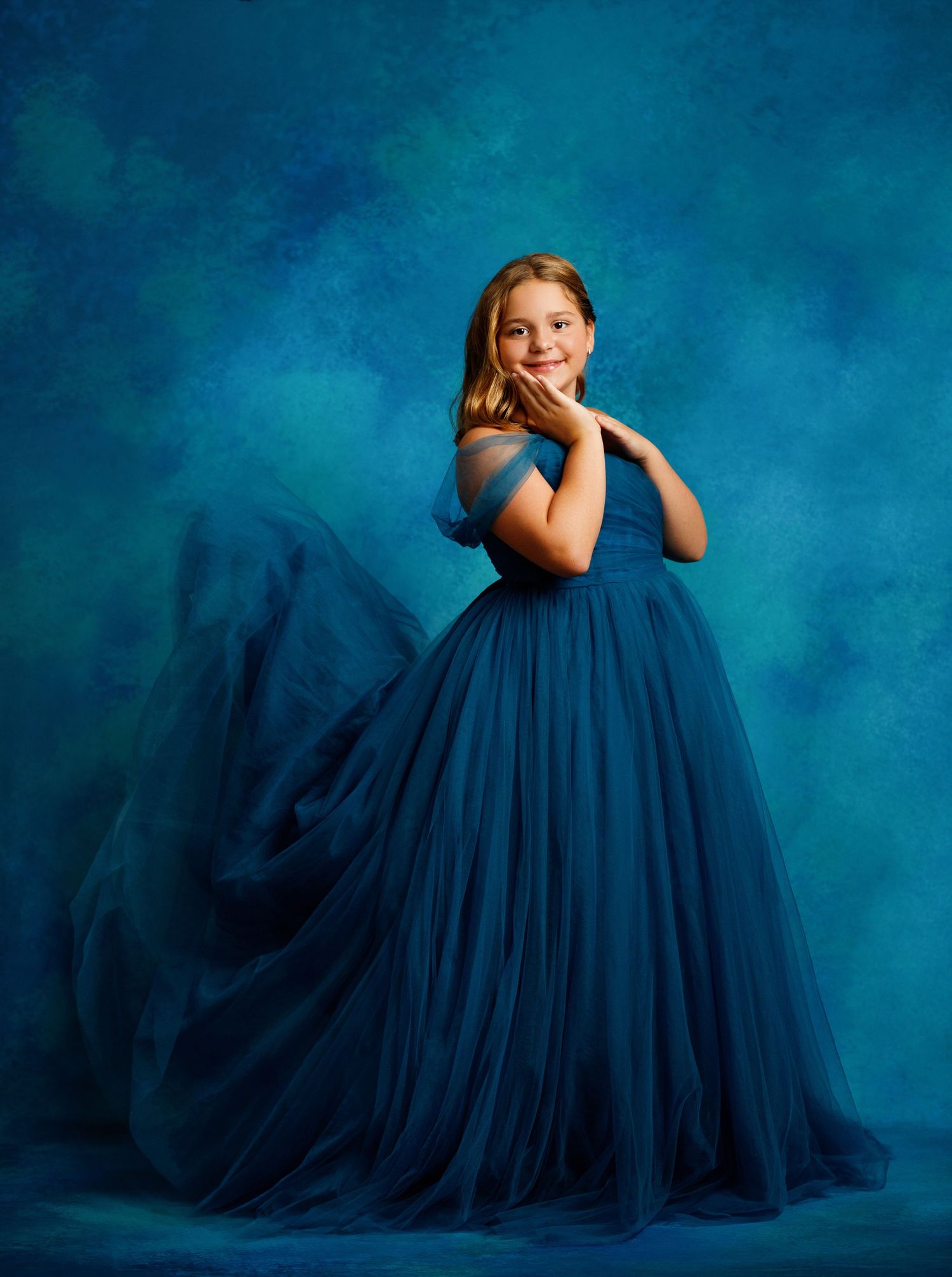 A vibrant teal ballgown dress with a full gathered skirt is shown against a warm autumn background.