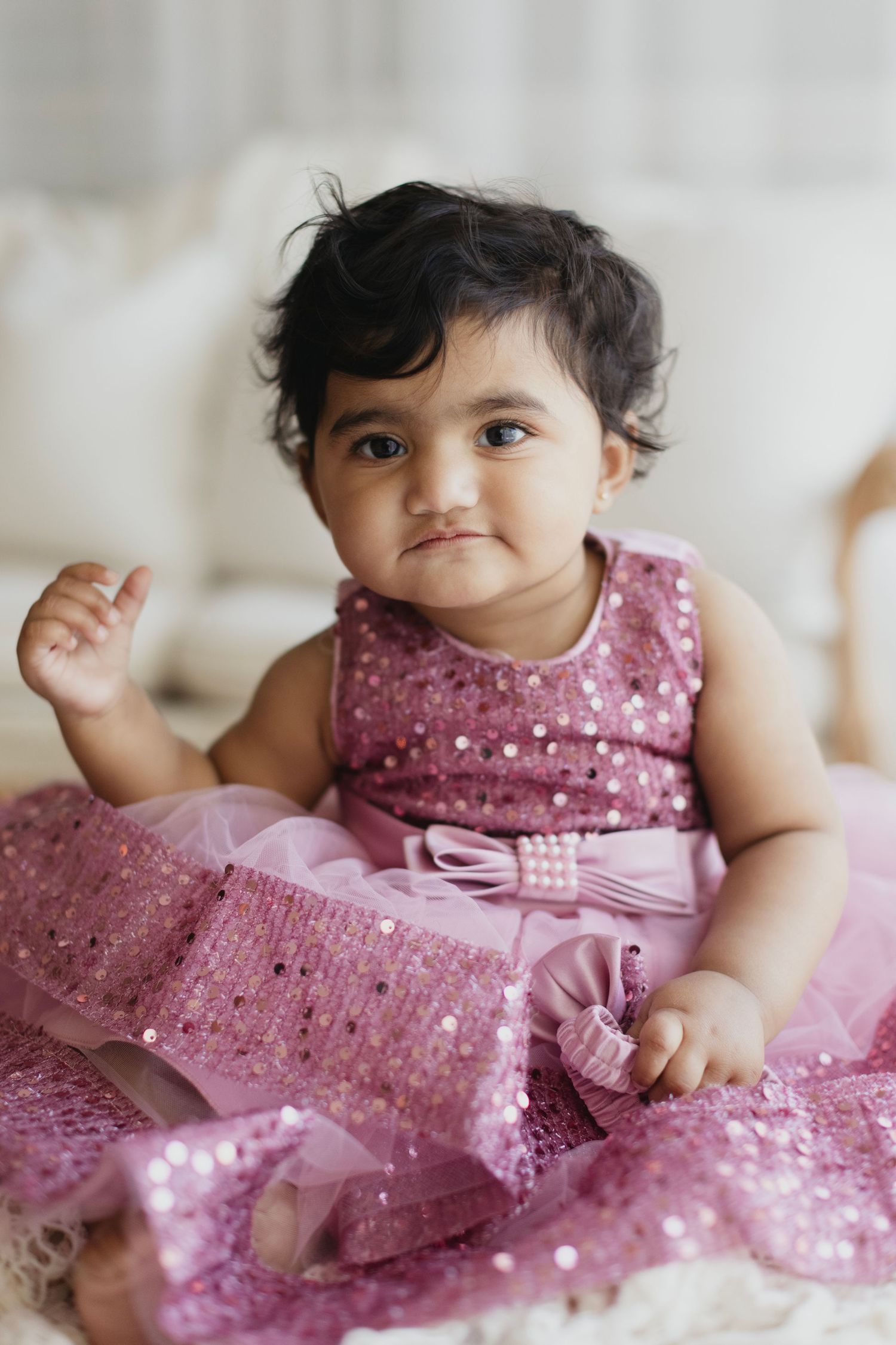 Adorable baby girl in a pink sequin tulle dress sitting and looking up with curious dark eyes.