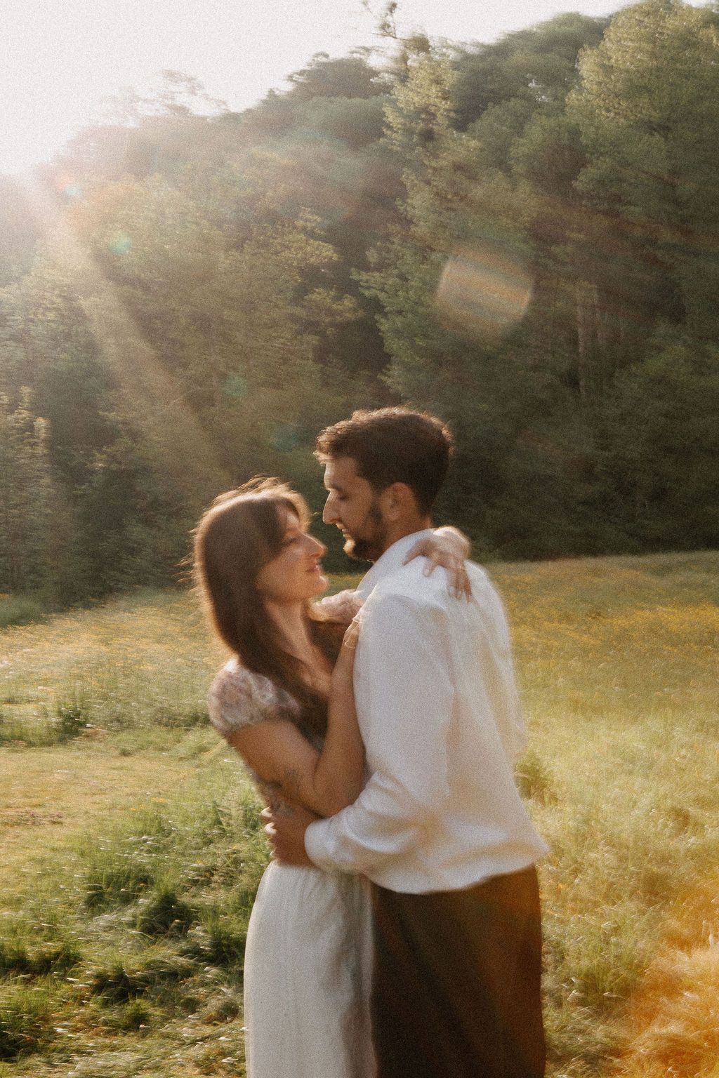 Couple holding each other close in a sun-drenched meadow with beautiful golden light flare.