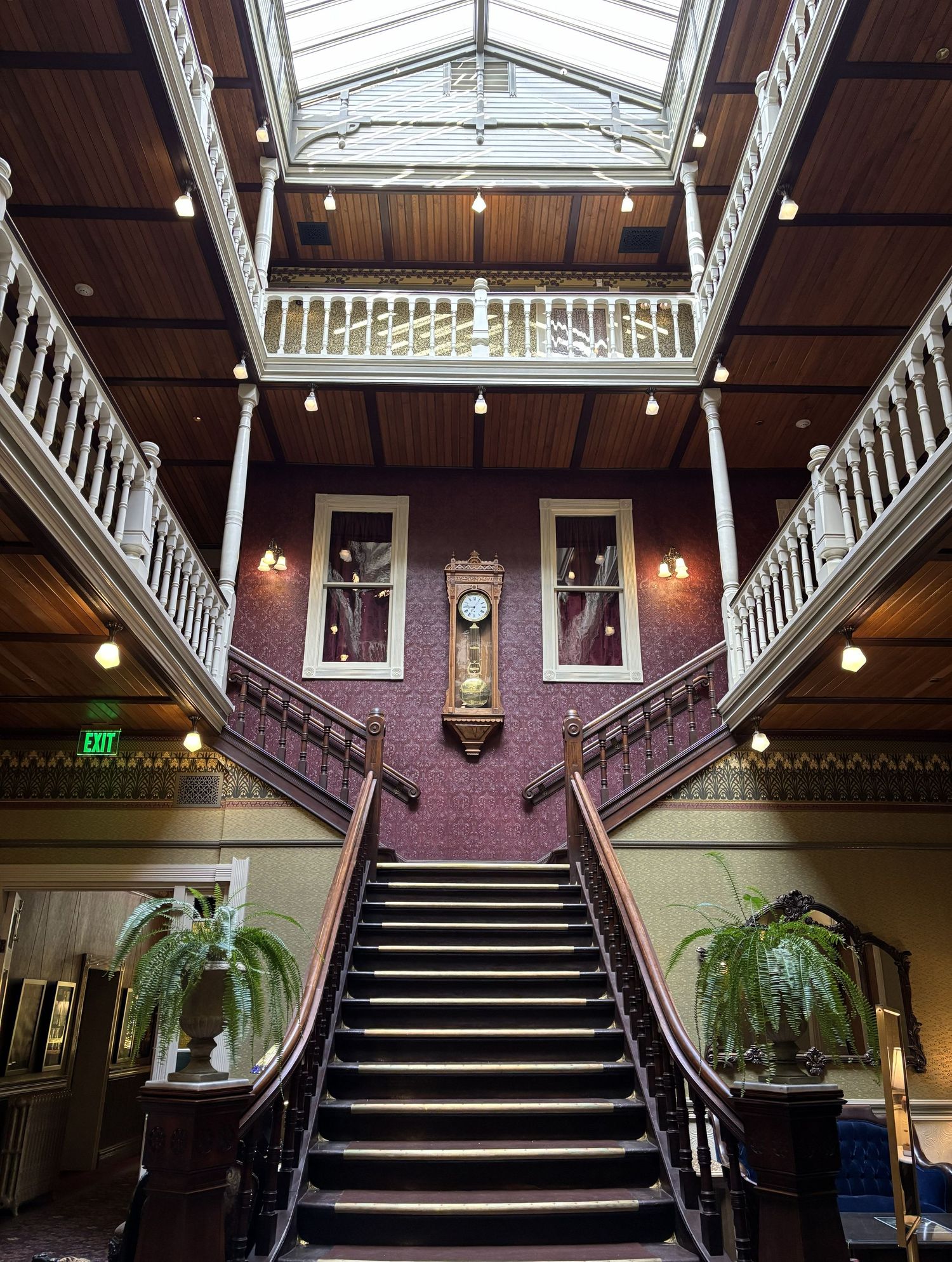 The grand Victorian hotel lobby of the Beaumont hotel with ornate staircase, skylight, balcony railings, wall clock, and decorative plants.