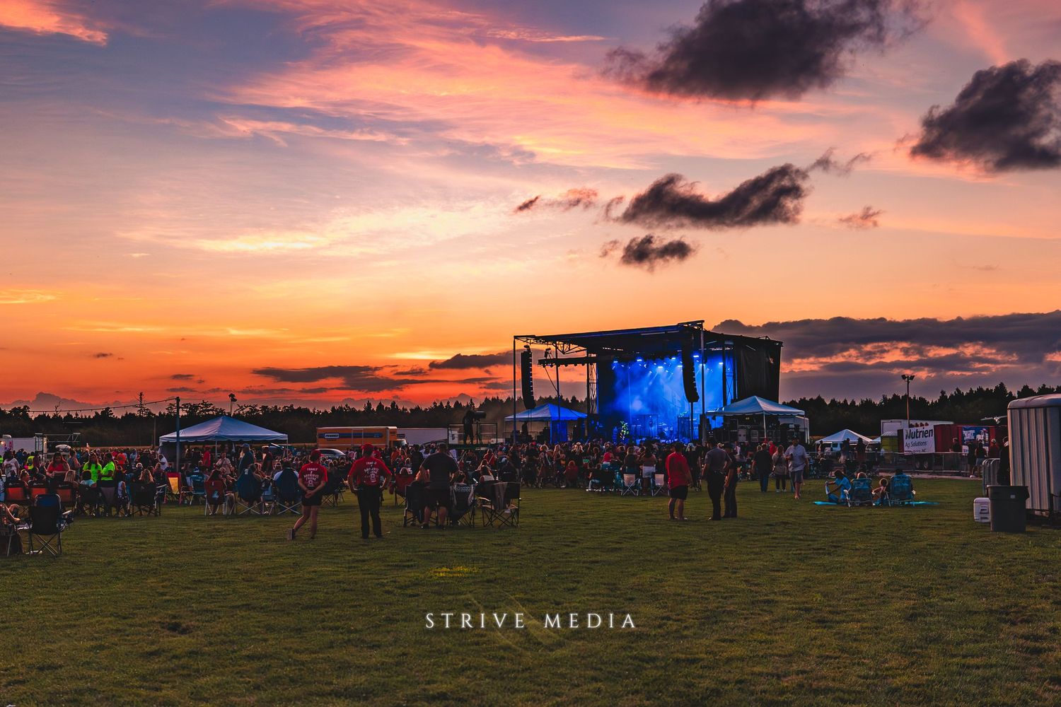 Outdoor music festival crowd enjoying a live stage performance at a stunning colorful sunset.