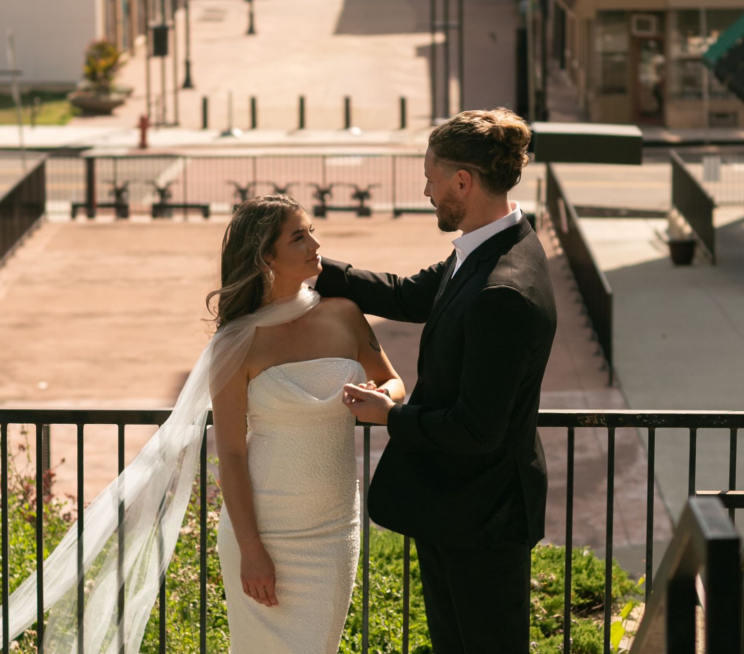 Bride and groom share a romantic moment on a balcony, with the groom tenderly touching the bride's shoulder.