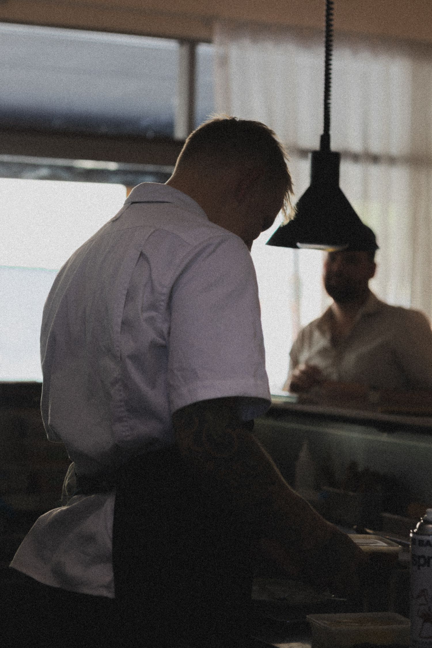 Chef in white shirt working at a restaurant kitchen counter with a pendant lamp overhead.
