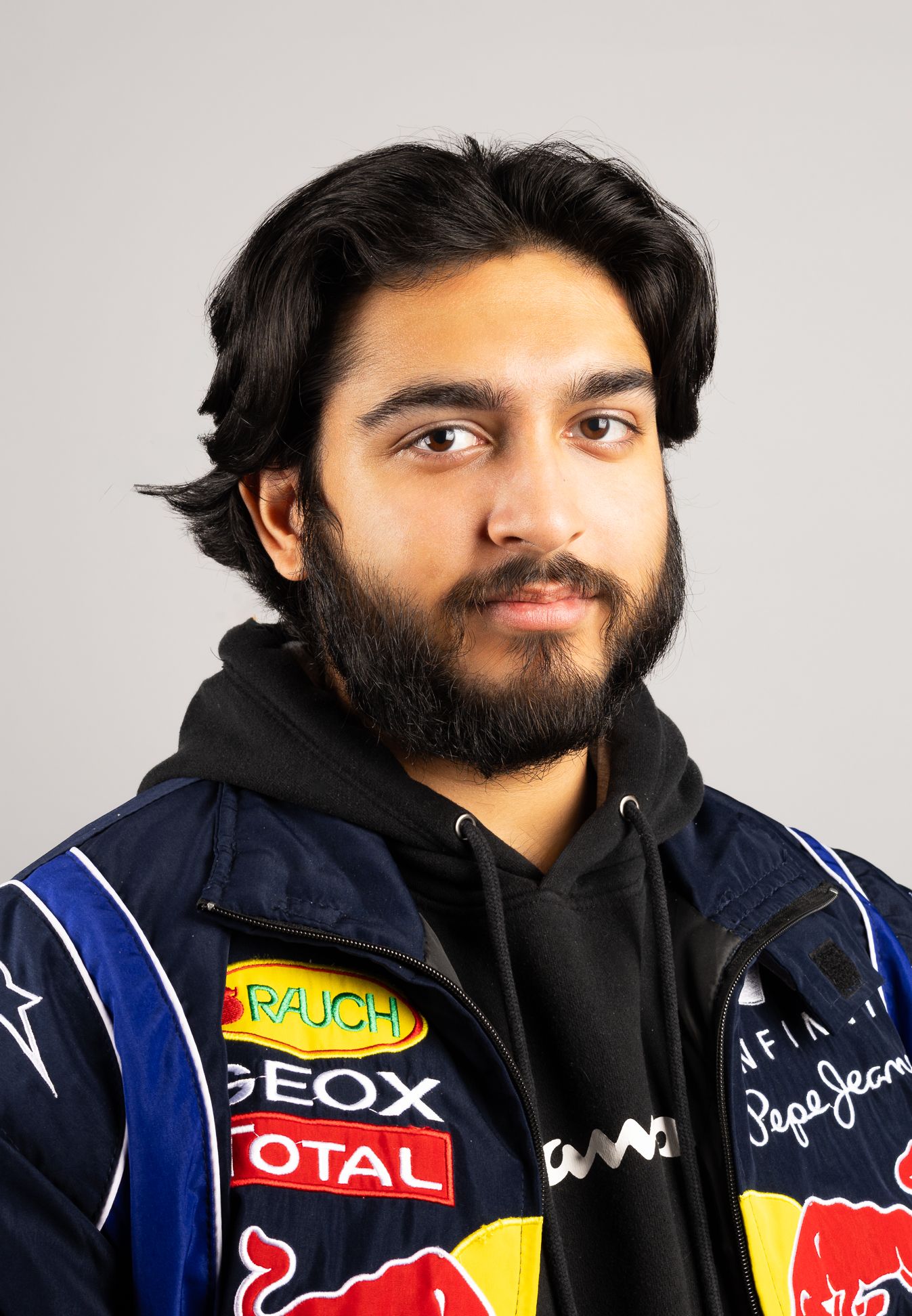 Image of a man in a racing jacket and hoodie, smiling and looking at the camera