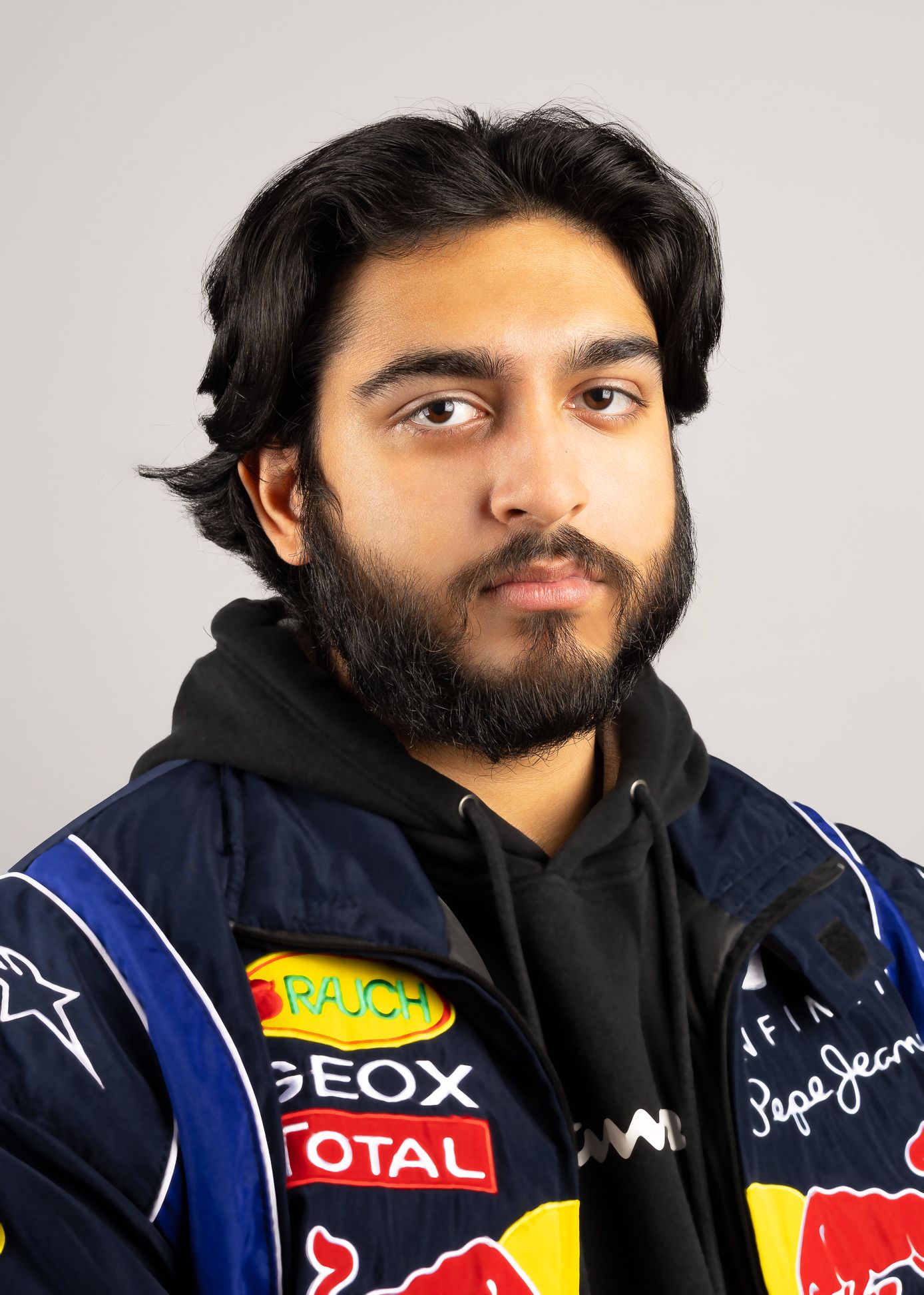 Image of a man in a racing jacket and hoodie, with no smile and looking at the camera