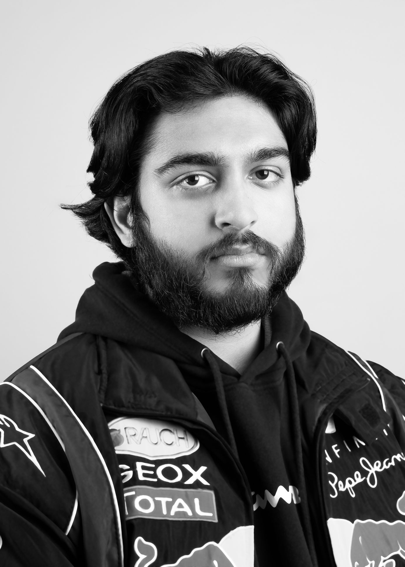 Black and white image of a man in a racing jacket and hoodie, neutral expression and looking at the camera