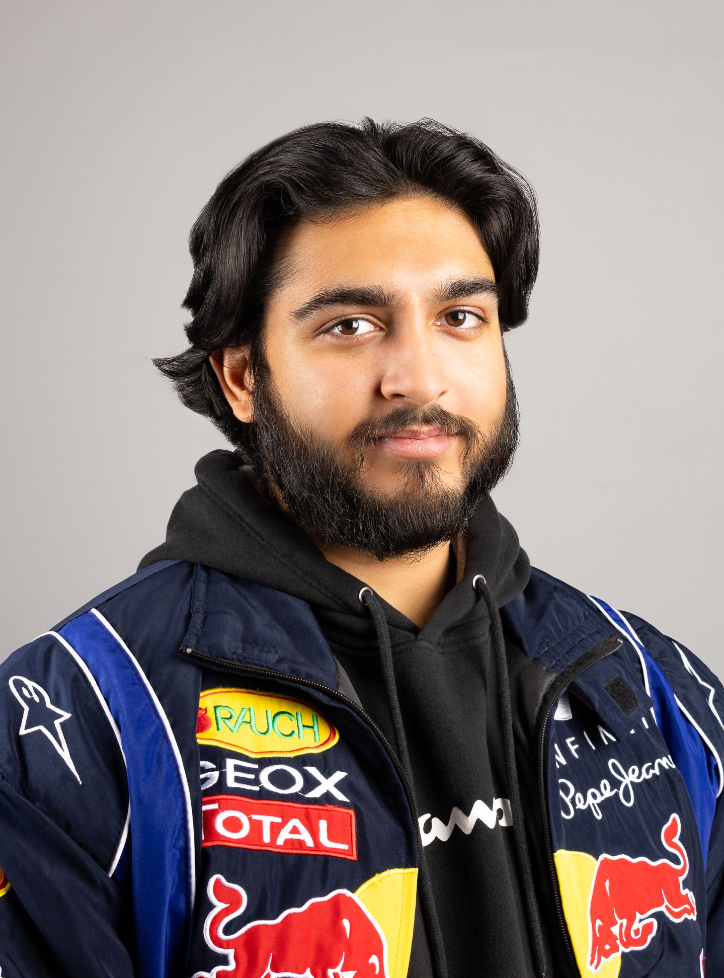 Image of a man in a racing jacket and hoodie, with a half-smile expression and looking at the camera