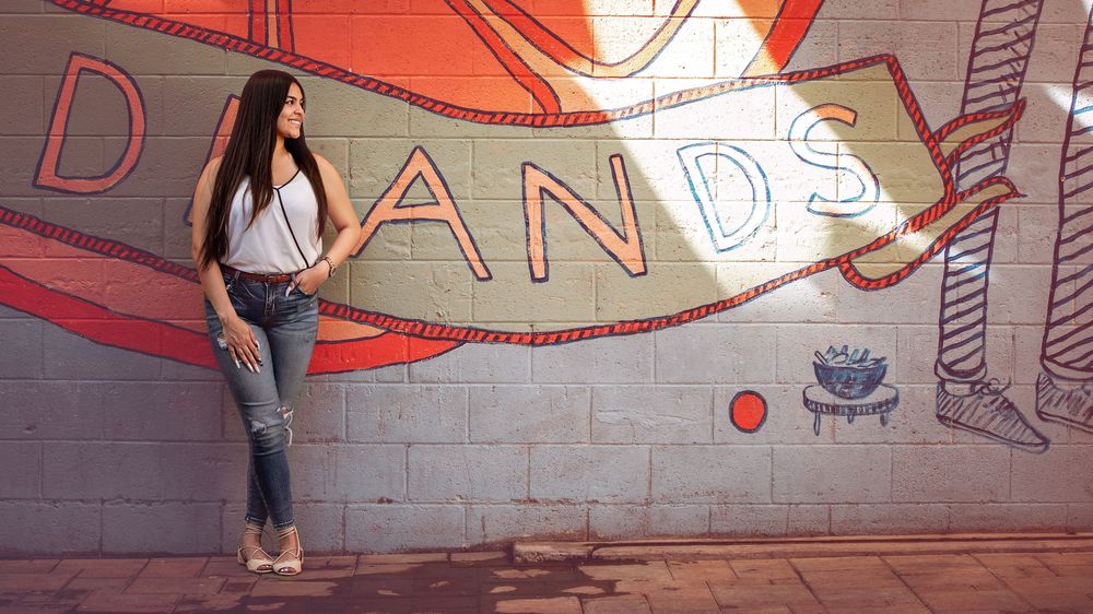 Young woman in jeans poses against a colorful graffiti mural wall outdoors.