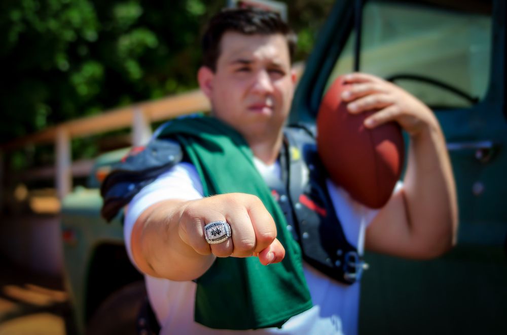 Football player proudly displaying a championship ring while holding a football outdoors.