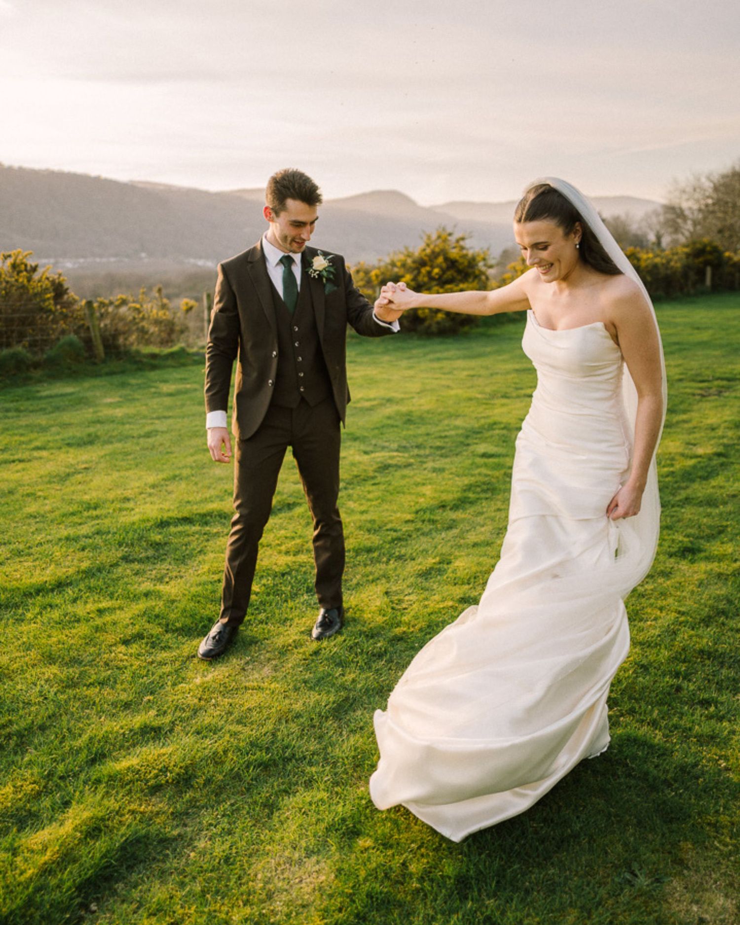 Black and white photo of bride and groom holding hands, showcasing floral lace wedding gown with flowing tulle skirt.
