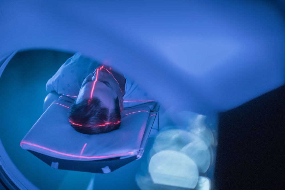 Patient receiving radiation therapy treatment in a modern medical linear accelerator machine with blue lighting.