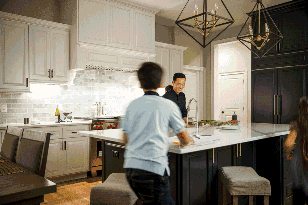 Modern kitchen with white marble island, dark cabinets, geometric pendant lights, and two people near the counter.