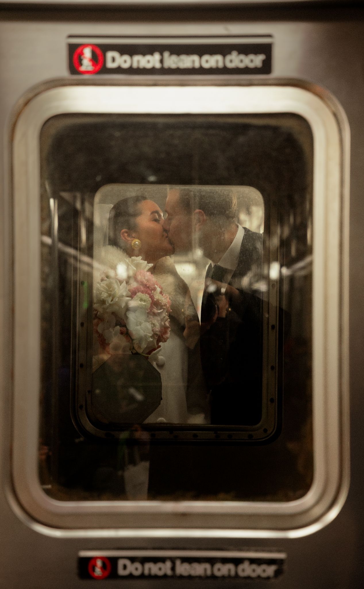 A bride and groom share a romantic kiss through a New York City subway car door window on their wedding day.