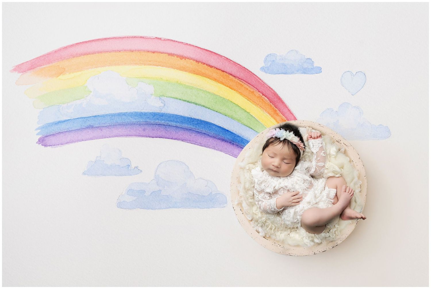 newborn photograph featuring watercolor rainbow with a wooded, fluff filled bowl with baby girl posed.