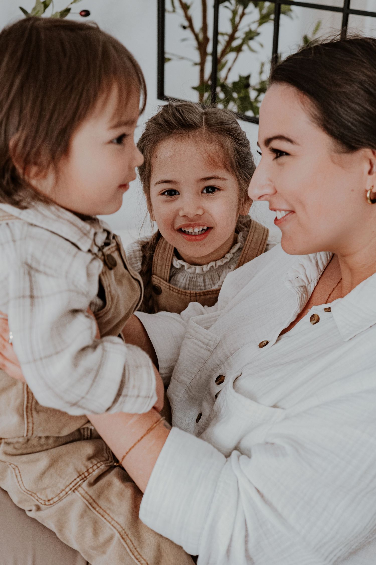 A smiling mother holds two young children, sharing a joyful moment together indoors.