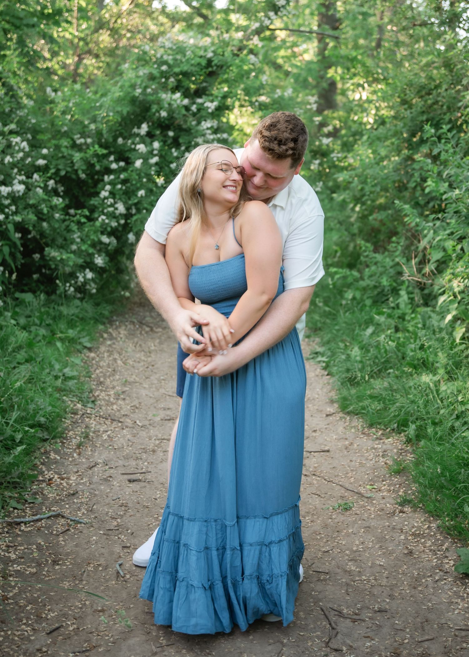 A couple embraces tenderly on a nature trail surrounded by lush green foliage in summer.