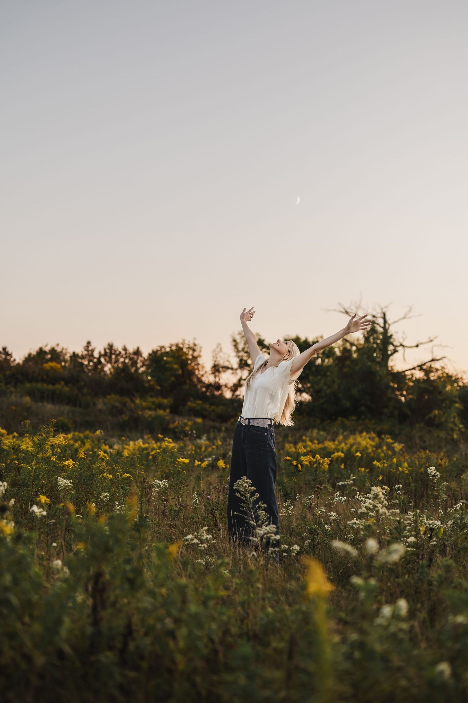 Michelle Hugill standing in a wildflower meadow at golden hour with arms raised in openness