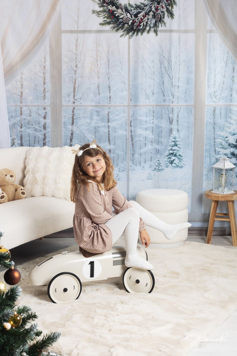 Vintage toy car by festive Christmas window with snowy winter forest scene and holiday wreath decoration.