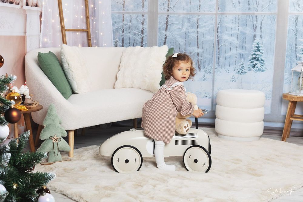 A child rides a vintage white toy car in a festive holiday setting with Christmas decorations.