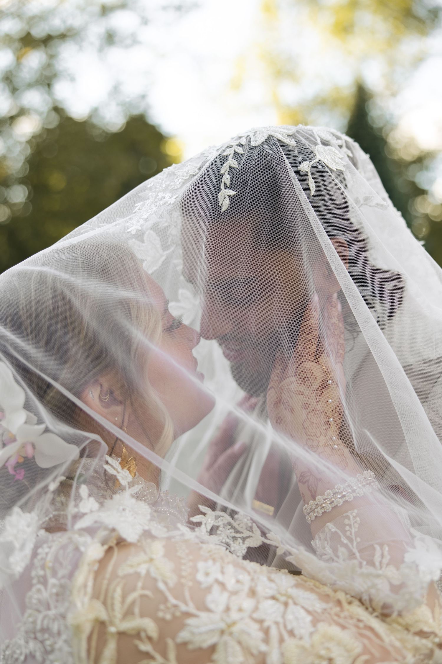 A romantic wedding moment captured through a delicate white veil in soft natural lighting.