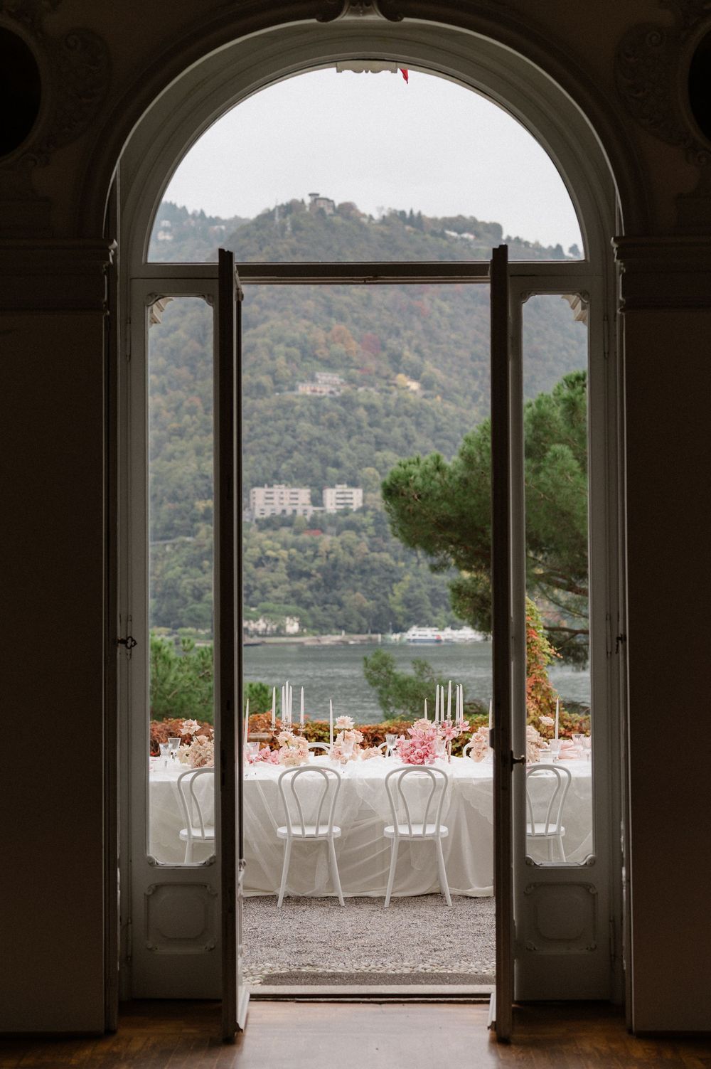 Elegant wedding reception tables set up on a terrace overlooking a scenic lake view through arched doorways.